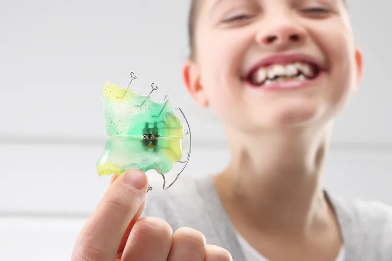 Child happily smiling while holding her orthodontic expanders